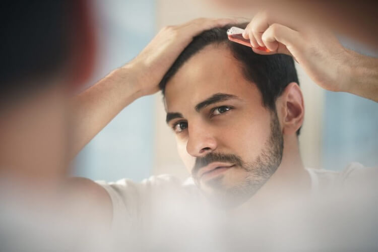Man looking in the mirror at his thinning hair line and applying a topical treatment to help containing finasteride. What are the results of finasteride? That depends on your treatment and dose. Check with a Happy Head dermatologist about a custom treatment. 