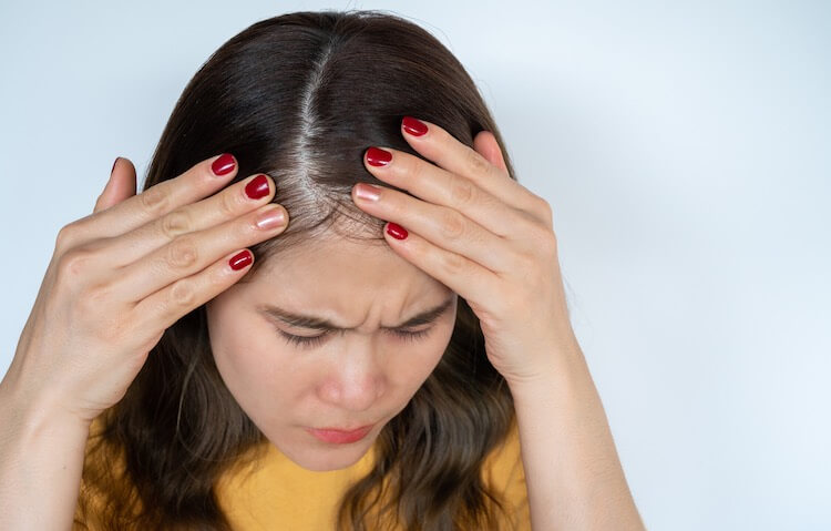 Woman looking at her hair closely trying to figure out how much hair she's lost. She's wondering if her female pattern hair loss can be reversed. Happy Head's board-certified dermatologists can help with custom topical hair growth treatments, oral medications, and more. 