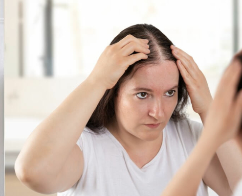 Woman looking at her part in the mirror, trying to decide if she's losing too much hair.