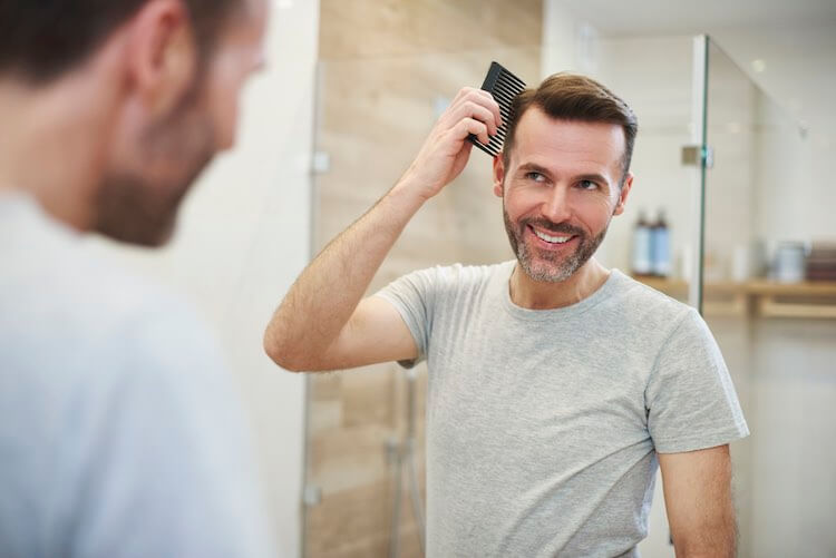 Man looking over his hair in the mirror while combing it back. He's excited about the hair growth results he's seeing with Happy Head topical solutions. 